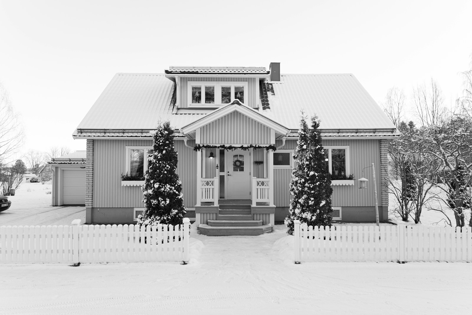 A snow-covered house with a white picket fence.